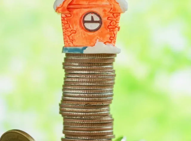 Mini house on stack of coins with green blur background.
